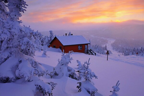 Una solitaria casa roja en un bosque de invierno en una colina en medio de una puesta de sol