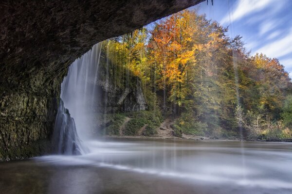 In autumn, a waterfall falls from a cliff into a lake