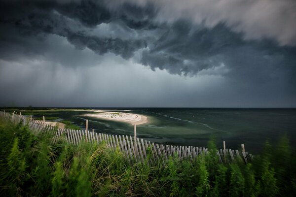 La nature se prépare à dormir: la mer, la clôture sur le rivage et les nuages dans le ciel