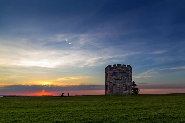 Un campo e una panchina con una torre sono fotografati al tramonto