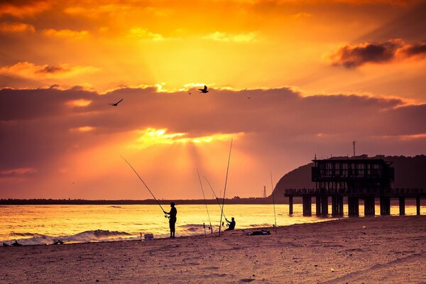 Sonnenuntergang am Meer. Mann fischt am Ufer