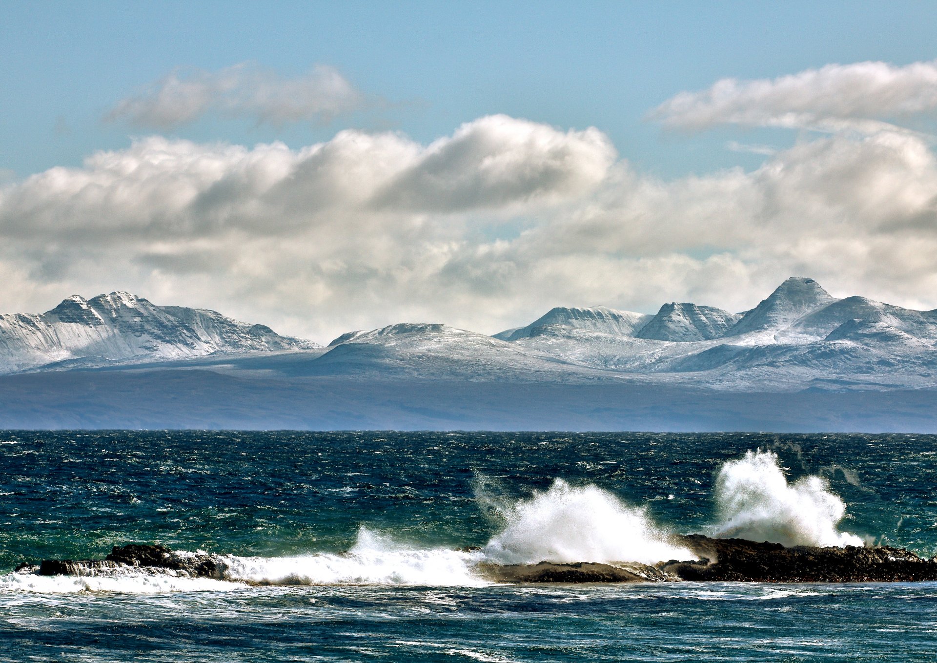 bahía olas rocas salpicaduras montañas picos cielo nubes