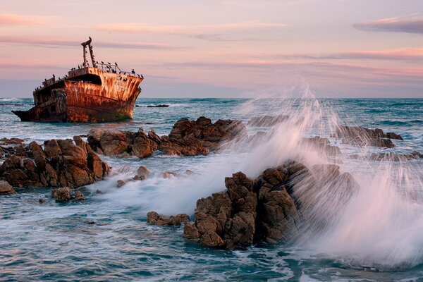 Barco entre el mar y las rocas en el fondo de la puesta de sol