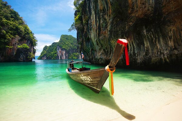 Boat on the white shore against the background of the green sea between the rocks