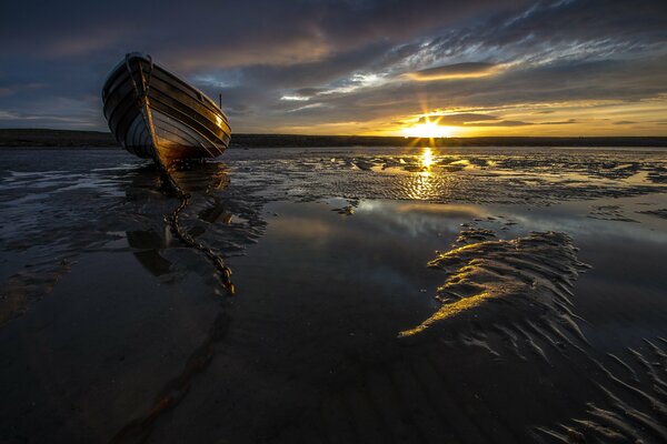 A boat stranded by the sea at sunset