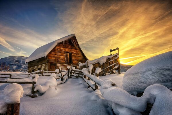 Ein Haus im Schnee vor dem Hintergrund von Sonnenuntergang und Schneeverwehungen
