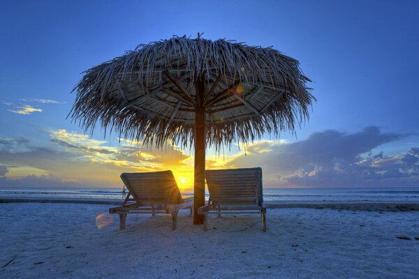 Chaises longues sous un parasol sur un fond de coucher de soleil