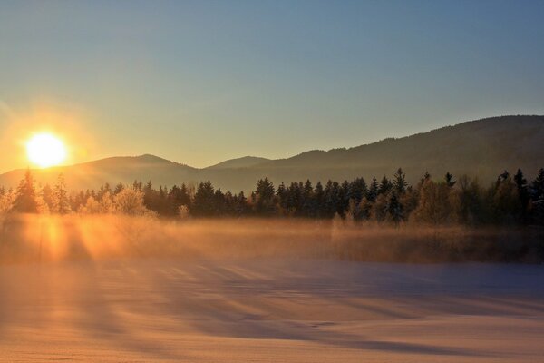 The sun is setting behind the mountain, the rays are in the fog